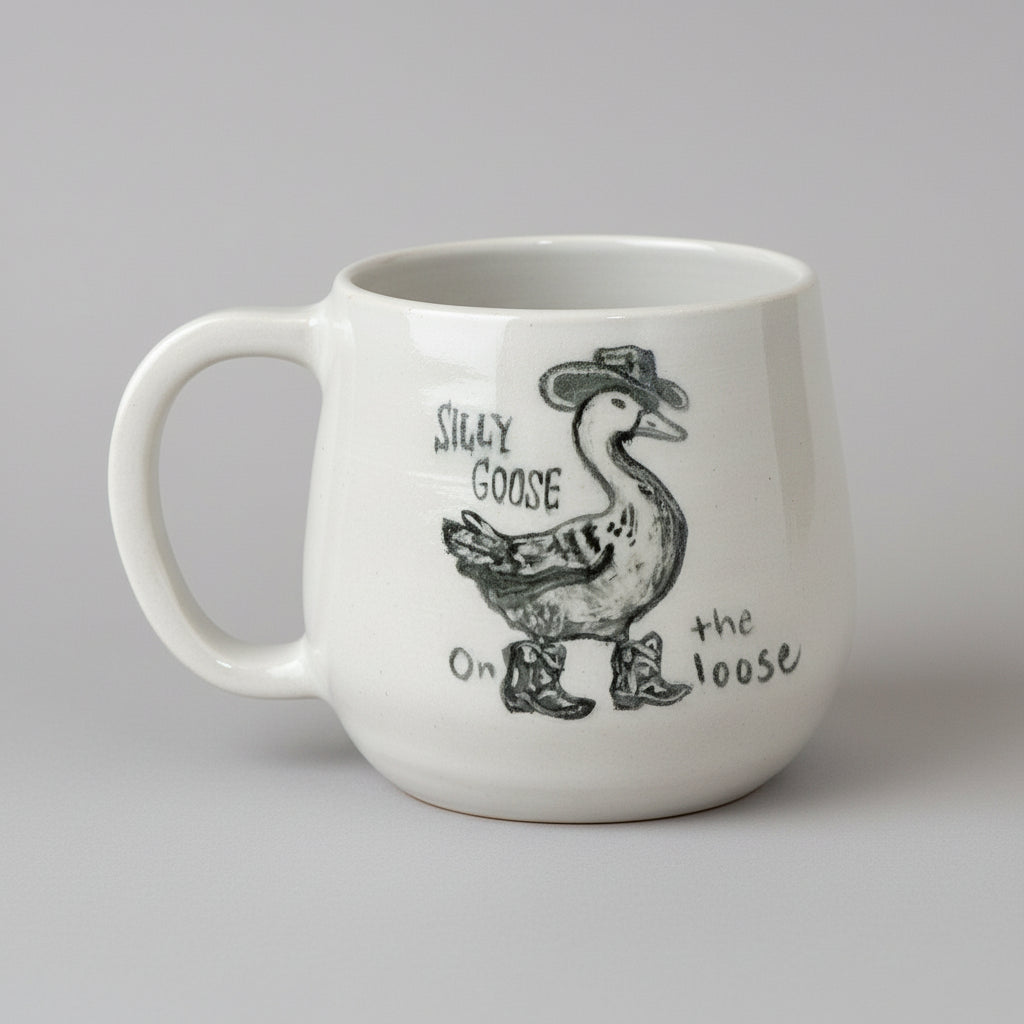 Ceramic mug with a cartoon goose wearing a cowboy hat and boots, and text 'Silly Goose On the Loose' on a gray background.